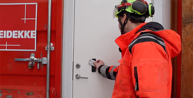 Bygningsarbeider bruker kortleser for adgang gjennom containervegg på byggeplass.