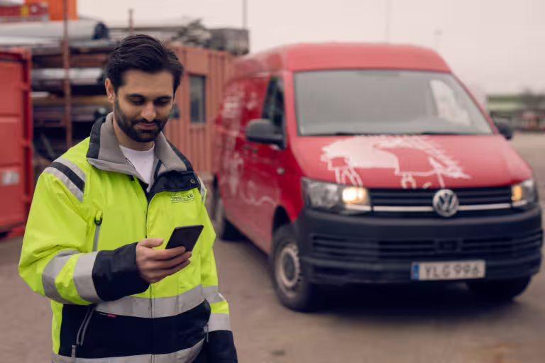 En man som står utanför sin bil och kollar sin milersättning på mobilen.